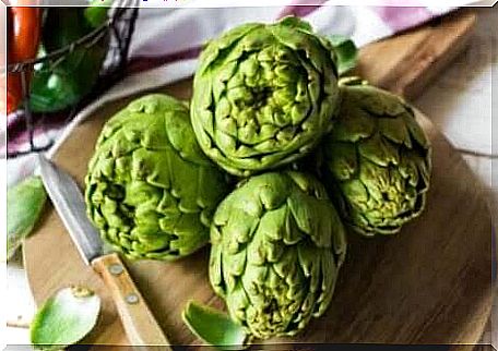 Green artichokes on a cutting board with a knife next to it